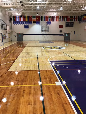 finished view of a full high school NCAA delux gymnasium refinishing with soild blue keys and a wide blue banner stnadrd logo and game court line markings after the resurfacing repair north Vancouver refinishing