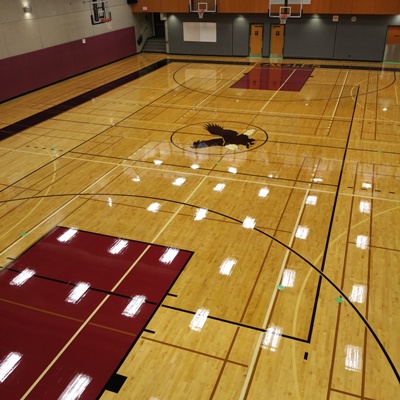 basketball gymnasium hardwood floor resurfacing company Vancouver BC high school basketball themed maroon and black with stined out international voleyball game court wide banner and block lettering transparencies